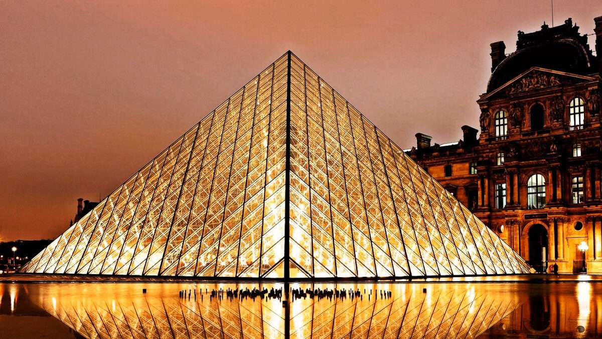 Banner mostrando o projeto arquitetônico da pirâmide de vidro do Museu do Louvre a noite e iluminado.